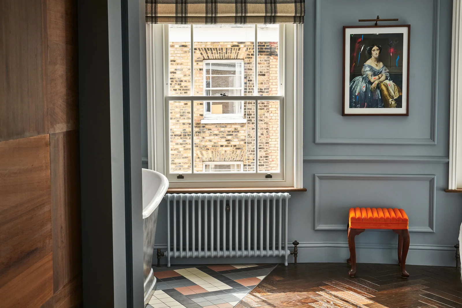 A blue panelled room with a sash window, an orange velvet stool and a framed portrait at The Lost Poet, Notting Hill
