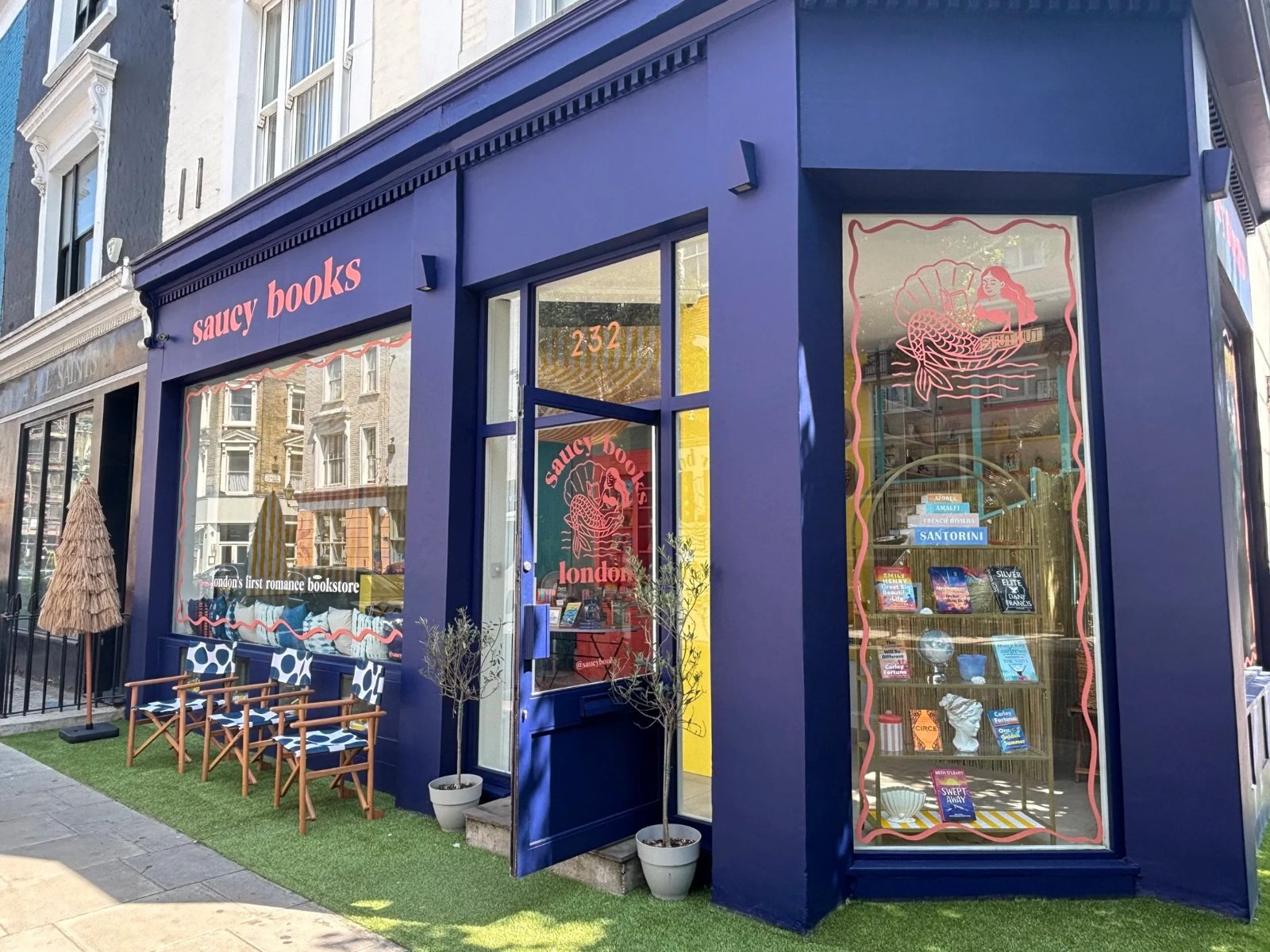 The navy shopfront of Saucy Books, its windows painted with a mermaid in a seashell for the Venus chapter