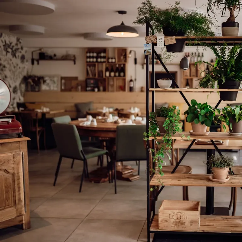 The dining room at L'Aillet, with wooden tables, green chairs and shelves of plants and wine crates
