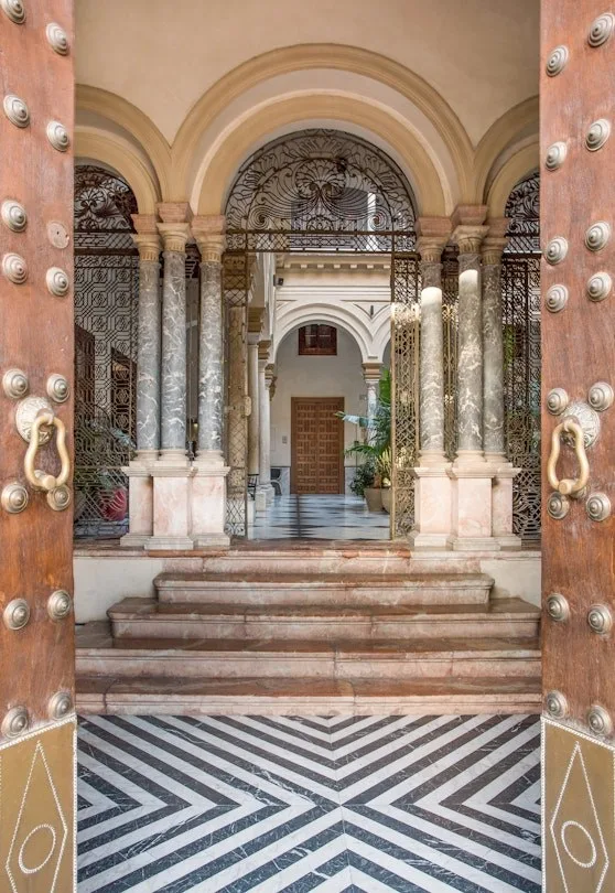 The entrance at Palacio Villapanés — studded timber doors opening onto marble columns and a striped stone floor