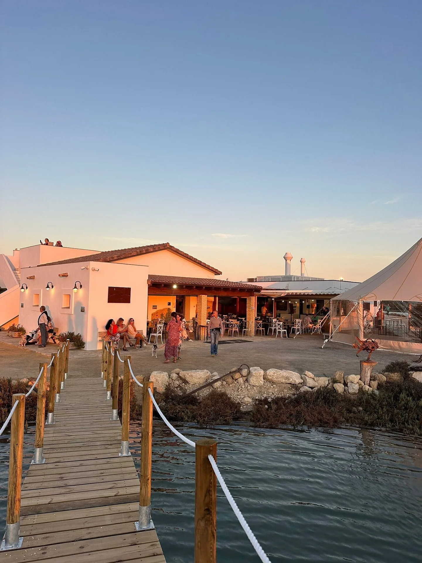 The buildings and terrace at Salina Santa Teresa at sunset, seen from the timber boardwalk across the water