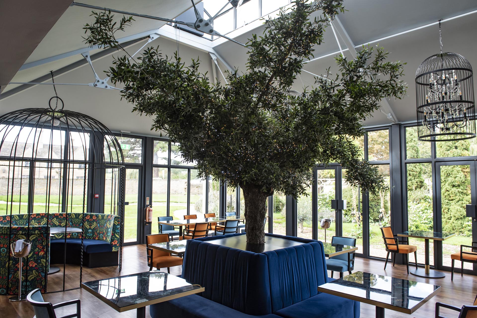 Prévost's bright orangery dining room with an artificial olive tree and birdcage chandeliers