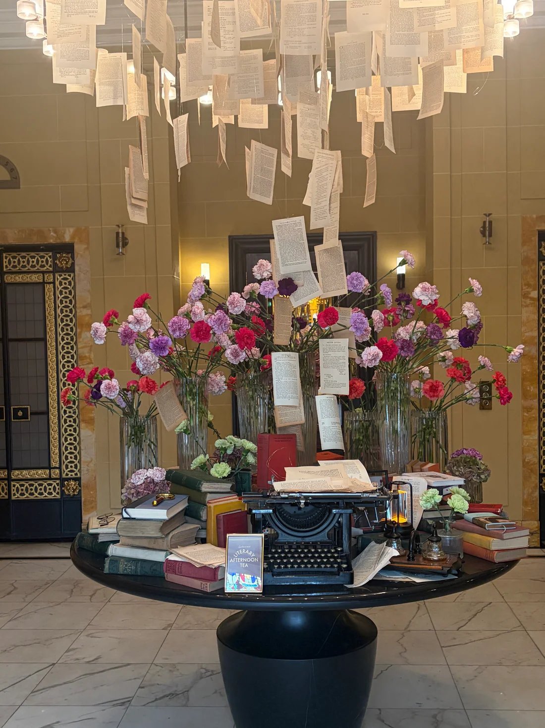 A literary display at the Hotel Café Royal: hanging book pages, carnations and a vintage typewriter on a round table