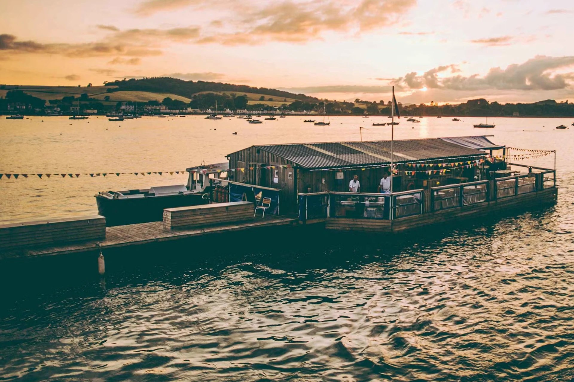 The timber shed of River Exe Café moored on the Exe Estuary at sunset, strung with bunting
