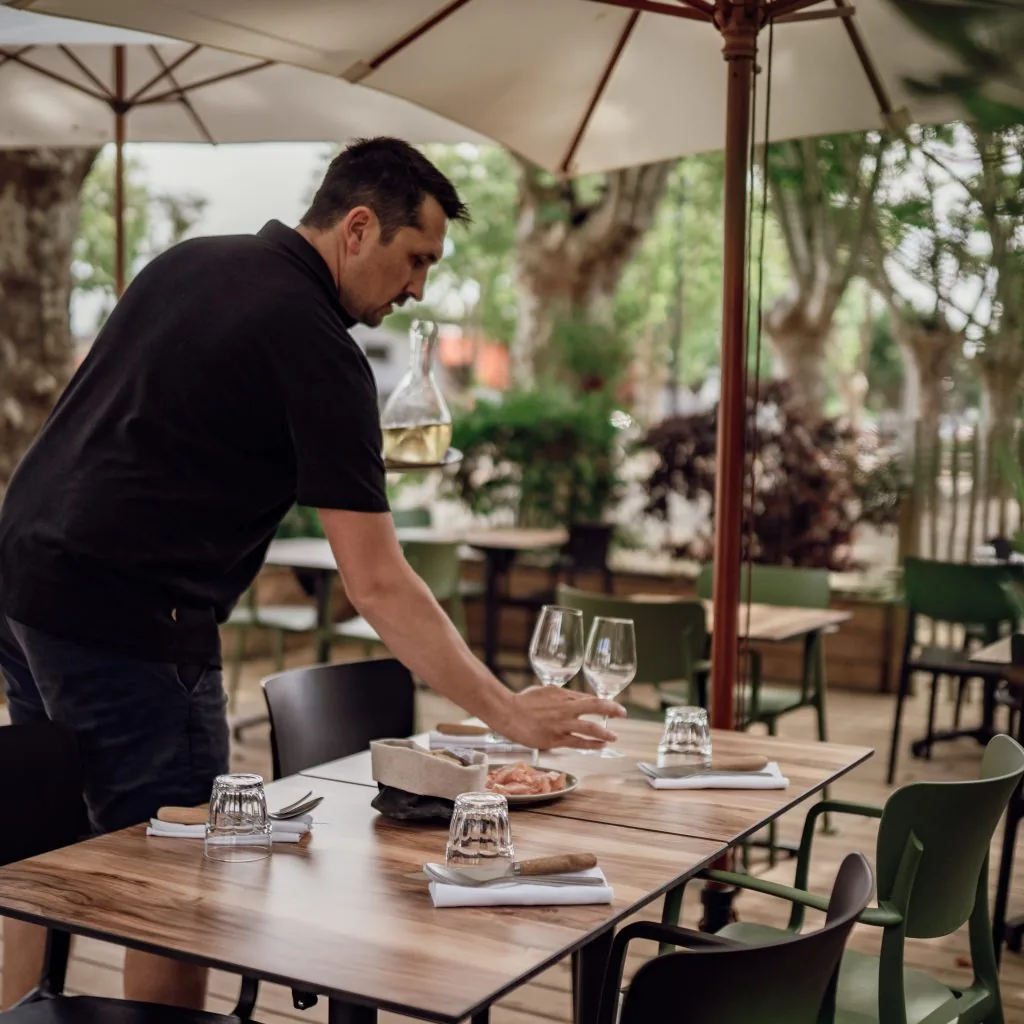 A member of staff laying a table on L'Aillet's terrace beneath the plane trees of Place Gambetta
