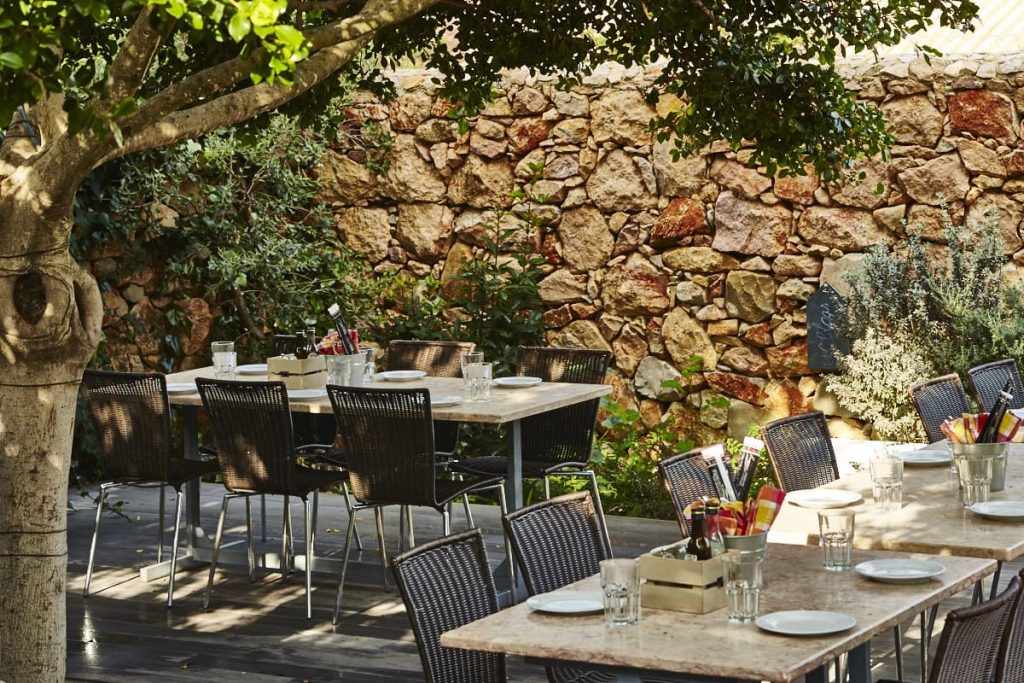 The garden terrace at Pizzeria Casavostra, tables laid beneath a tree against an old stone wall