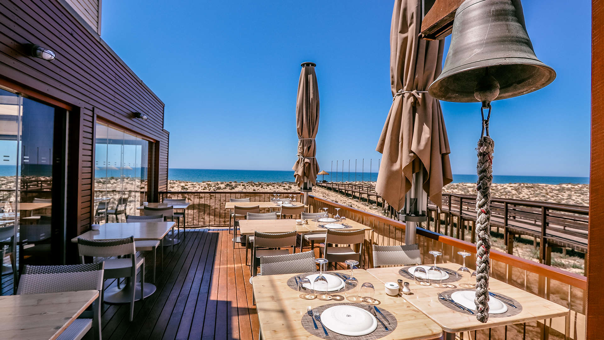 The terrace at 2 Passos, laid tables and a ship's bell looking out over the dunes to the Atlantic