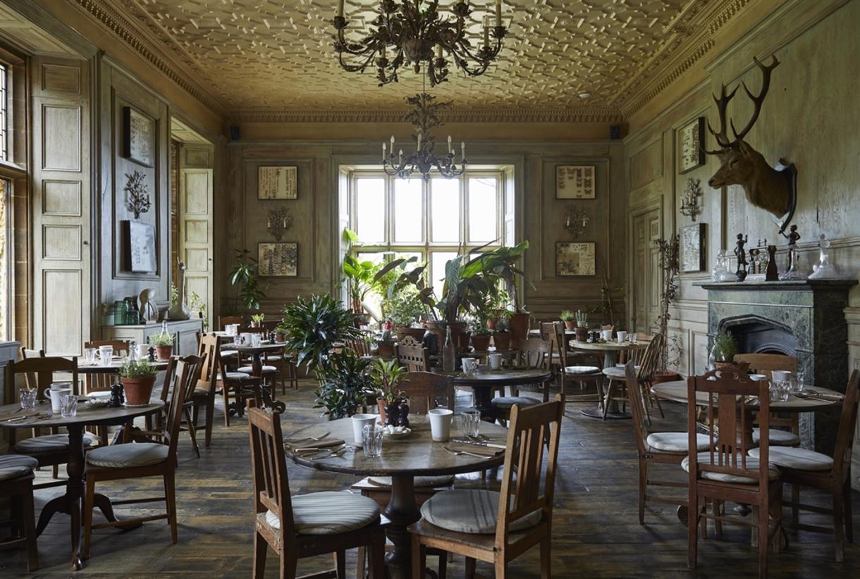 The panelled dining room at The Pig at Combe with chandeliers, plants and wooden tables