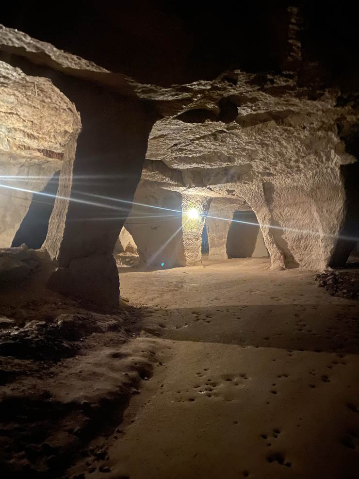 Hand-cut limestone pillars and vaulted chambers lit by a lamp inside Beer Quarry Caves