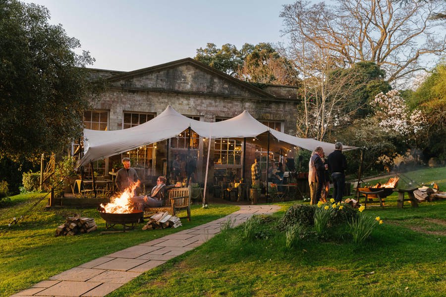 Guests around fire pits outside The Folly in the grounds of The Pig at Combe