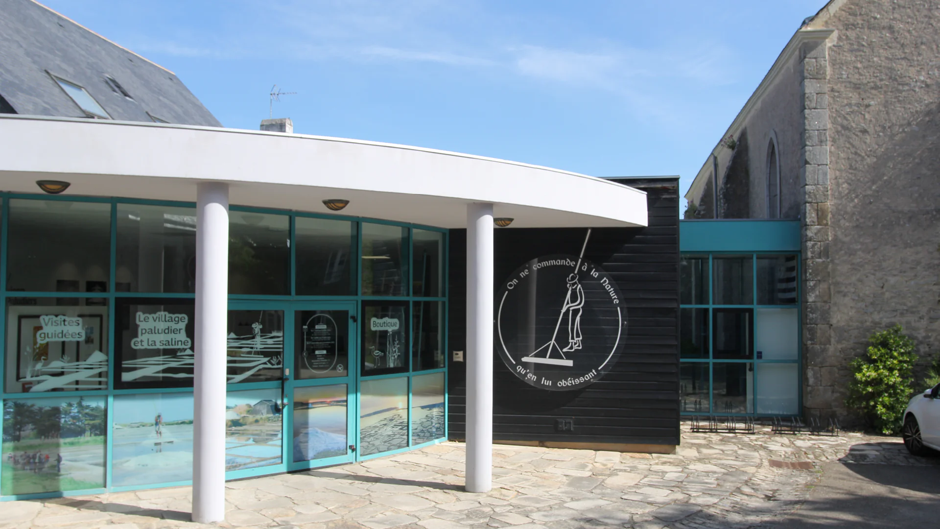 The curved white canopy and teal-framed glass entrance of the Maison des Paludiers in Saillé