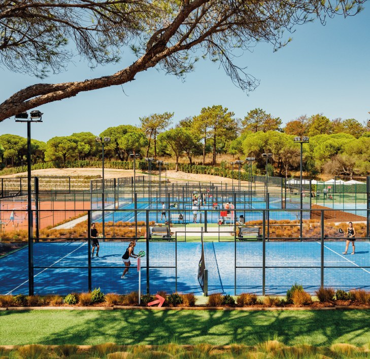 Players on the blue padel courts at The Campus, Quinta do Lago, beneath umbrella pines