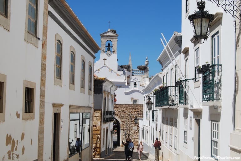 A white street in Faro's old town leading towards the bell tower of the Arco da Vila