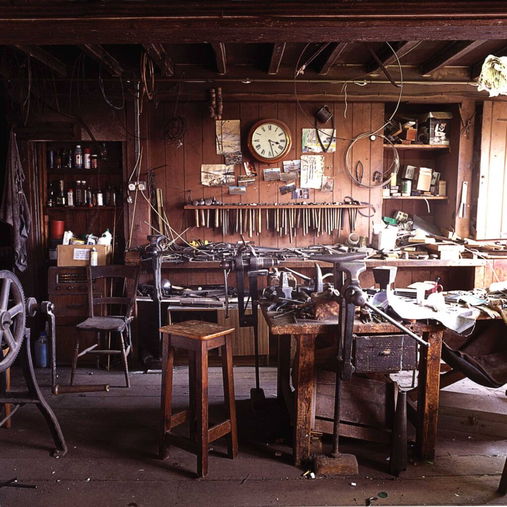 The Hart Silversmiths workshop in the Old Silk Mill, Chipping Campden — a wall of hand tools beneath a station clock above crowded workbenches