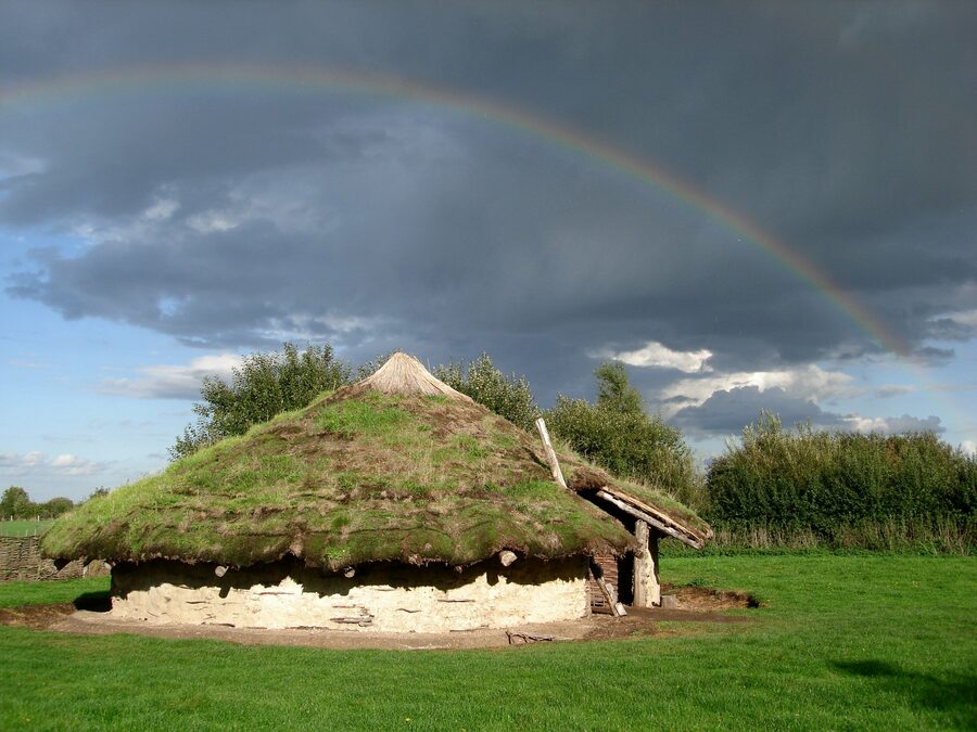 Reconstructed Bronze Age roundhouse at Flag Fen beneath a rainbow and dark Fenland sky