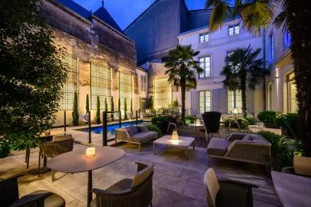 The Villa Grand Voile courtyard terrace at dusk, lit lanterns on low tables beside palms and the pool