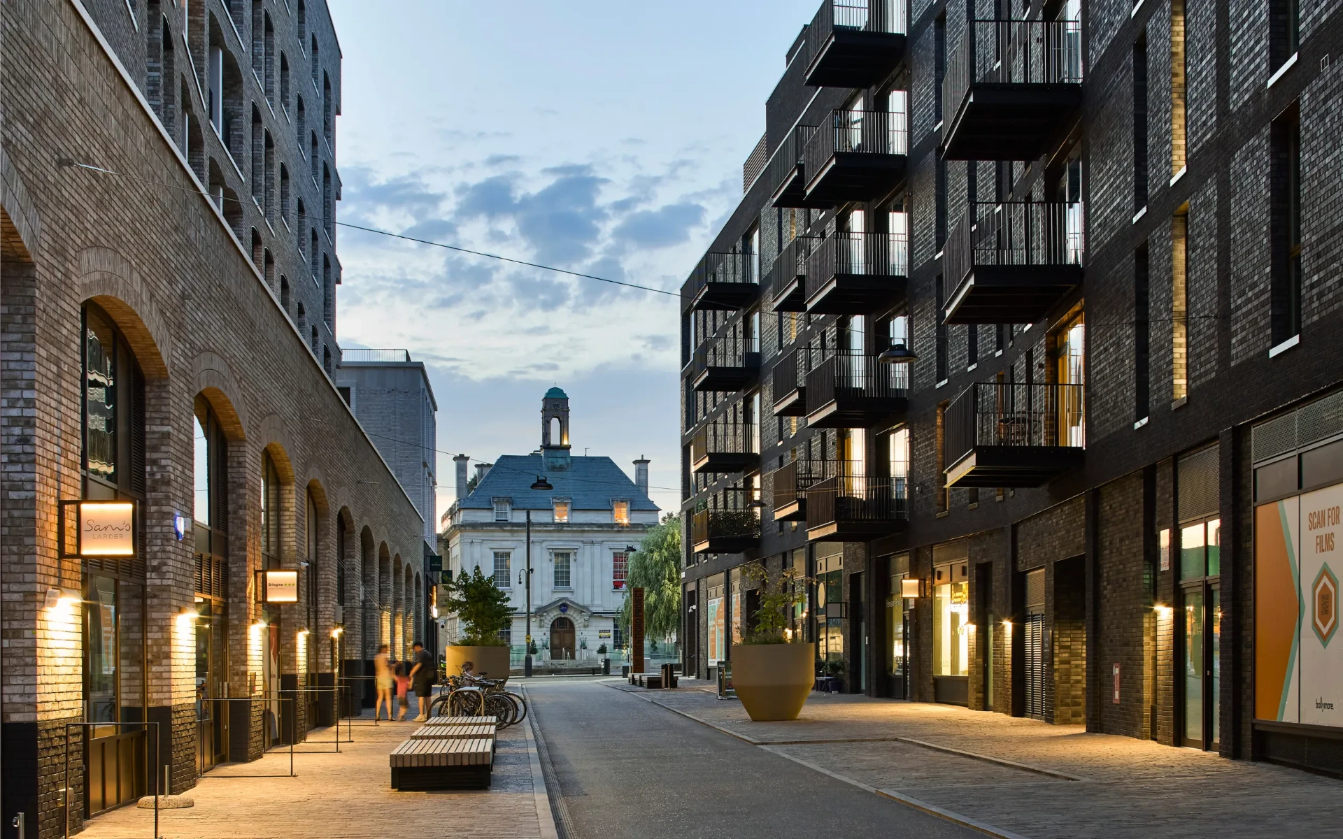 A pedestrian street through The Brentford Project with brick arches, apartments and waterfront businesses