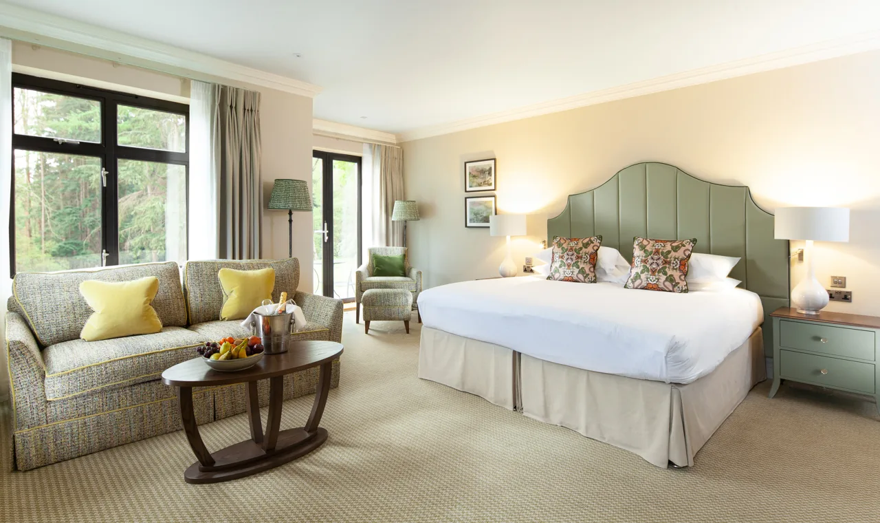 A Foxhills bedroom with a green upholstered headboard, patterned sofa and full-height windows onto the woodland