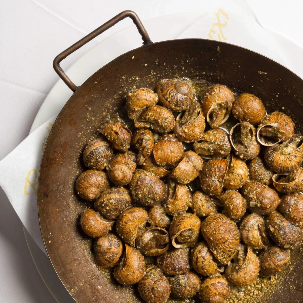 Snails in a metal pan at El Racó del Cargol, seasoned and served on a white plate