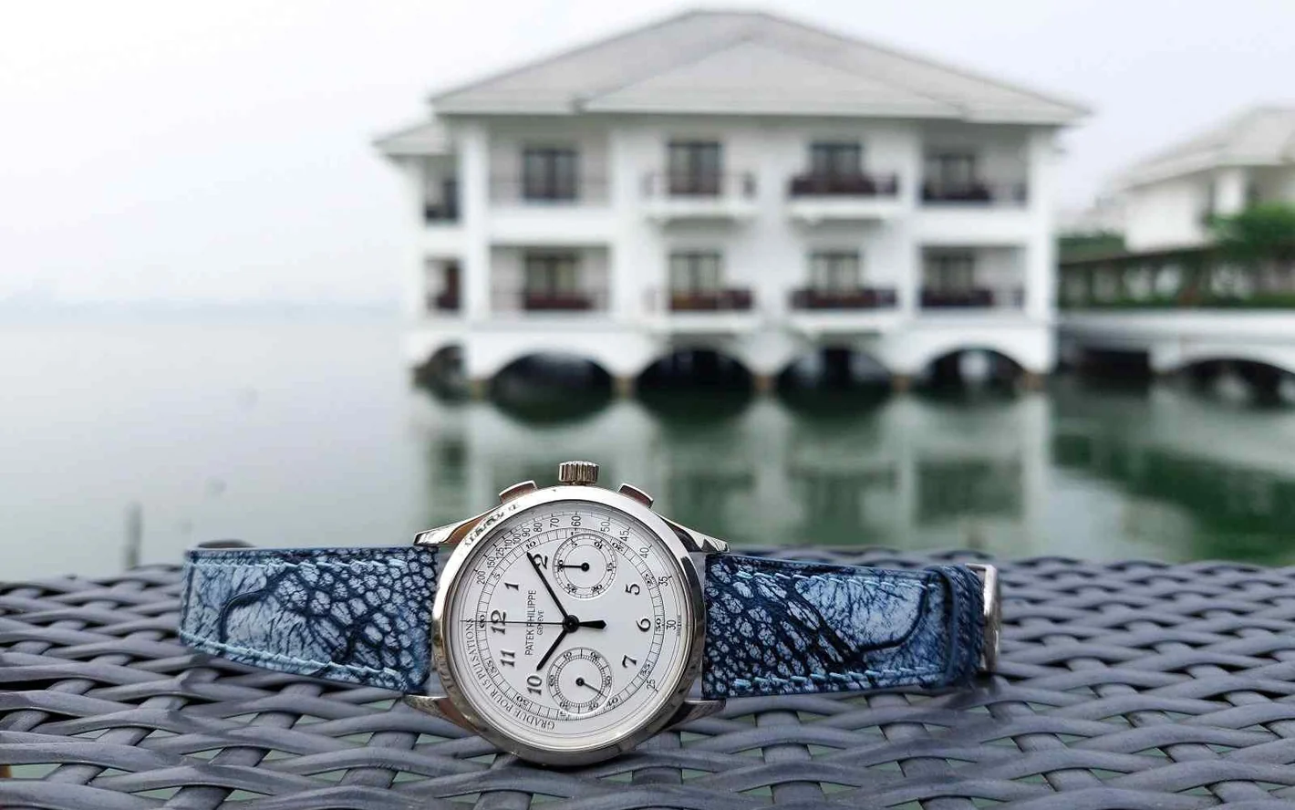 A watch fitted with a blue Atelier KAI leather strap on a woven table beside the water