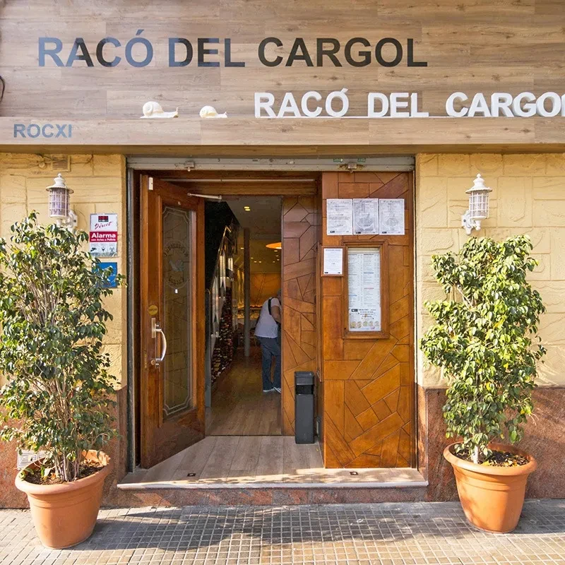 The entrance to El Racó del Cargol on Carrer Doctor Martí i Julià, with wooden doors, potted plants and the restaurant name above