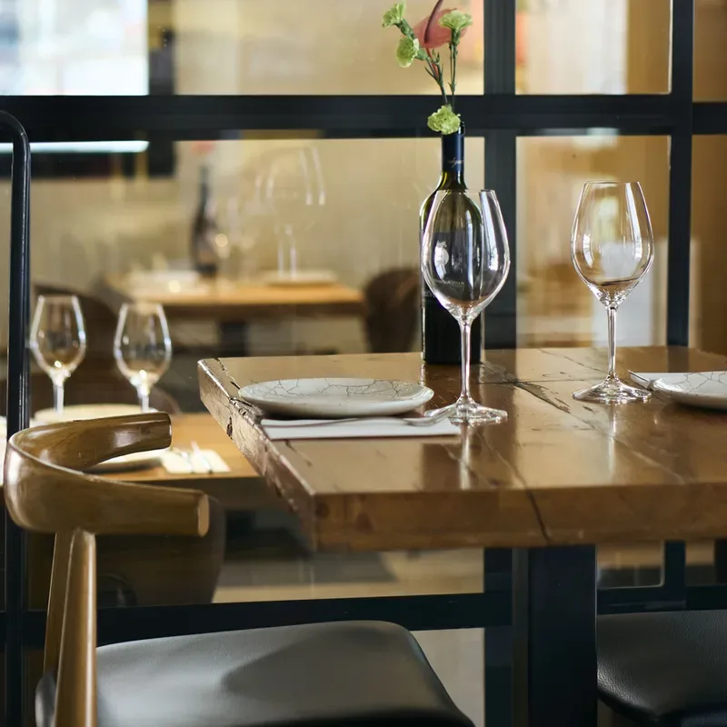 A table set for two at El Disparate — reclaimed timber, wine glasses and a single stem in a bottle