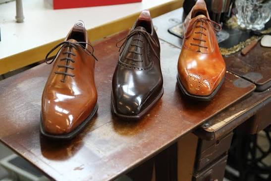 Three polished leather shoes displayed on a wooden workbench at Fumu
