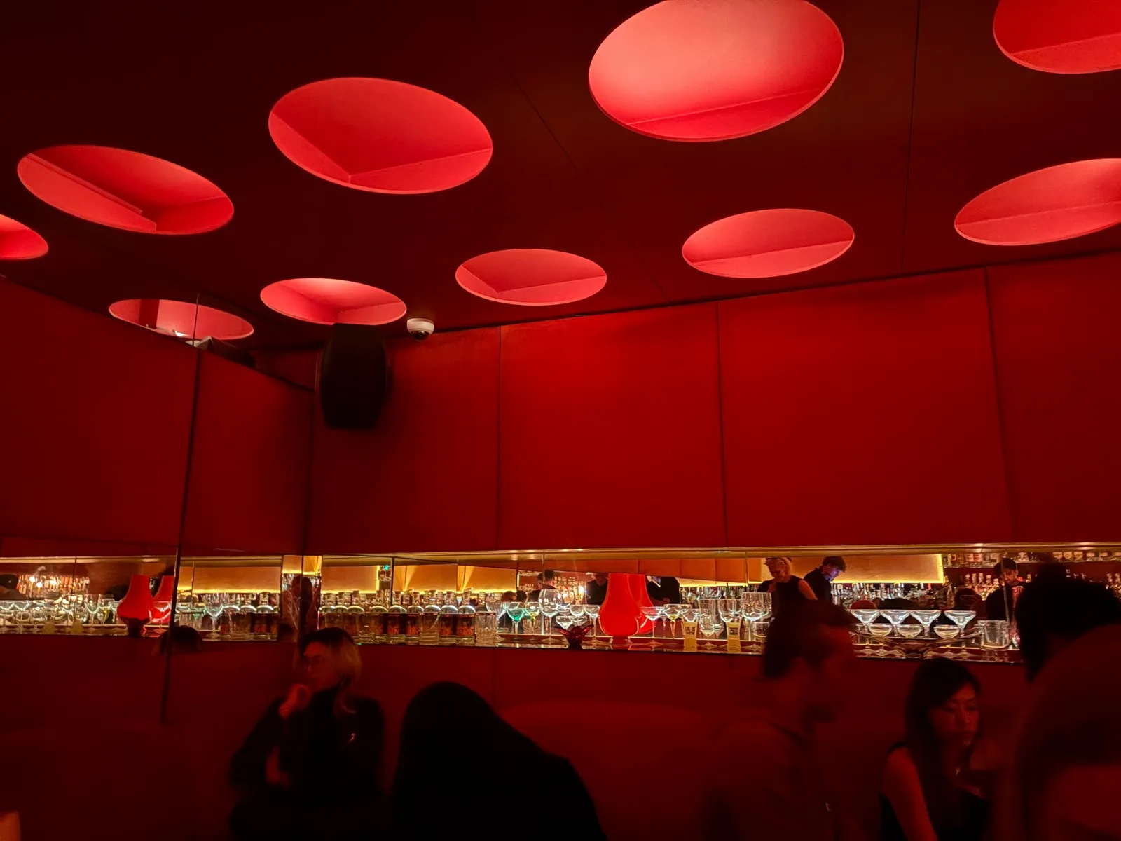 Glowing red ceiling lights above the velvet banquettes and mirrored bar at Naked & Famous, beneath zēphyr on Portobello Road