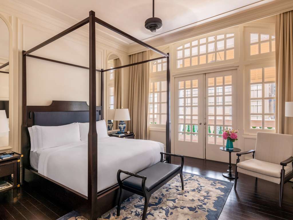 A suite at Raffles Singapore with a four-poster bed, tall windows and veranda doors
