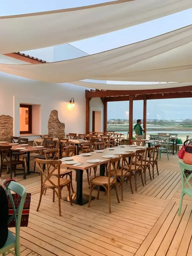 The dining room at Salina Santa Teresa, long timber tables under canvas sails looking out over the marsh
