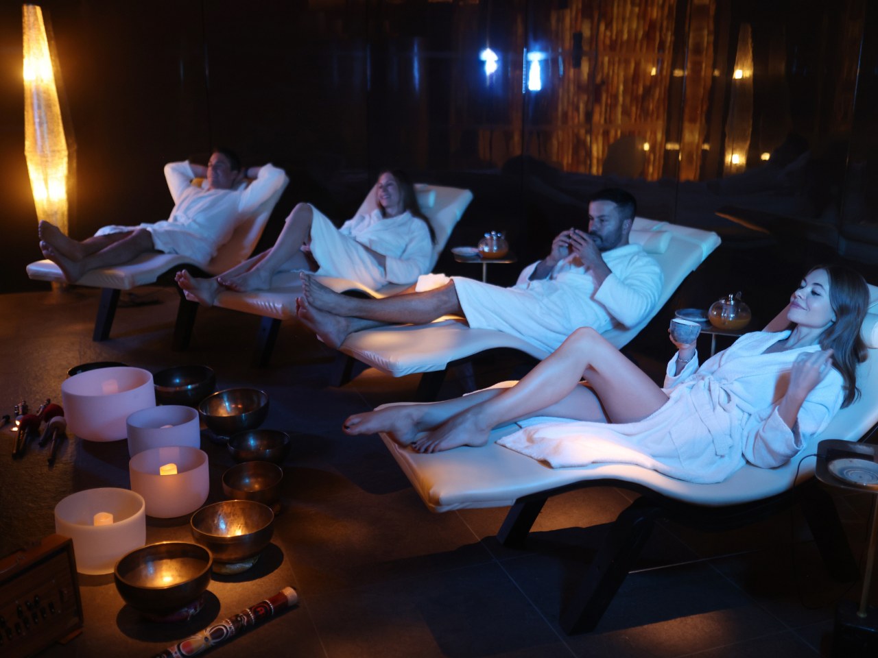 Guests in white robes on loungers in the candlelit relaxation room at Cloud Twelve, with singing bowls on the floor