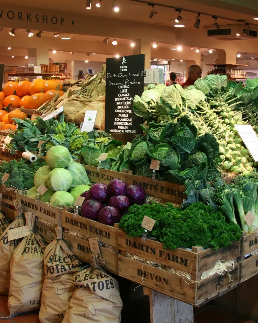 The vegetable display at Darts Farm, wooden crates stamped Darts Farm Devon piled with cabbages, kale and leeks