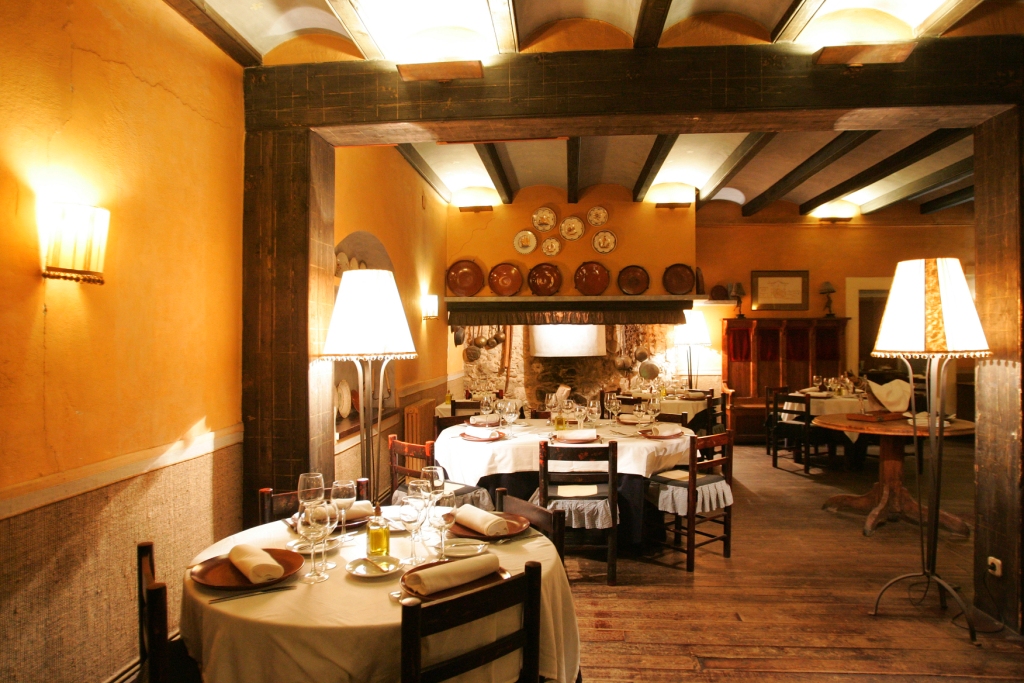 A warm orange dining room at Can Travi Nou with timber beams, a fireplace and tables set for service