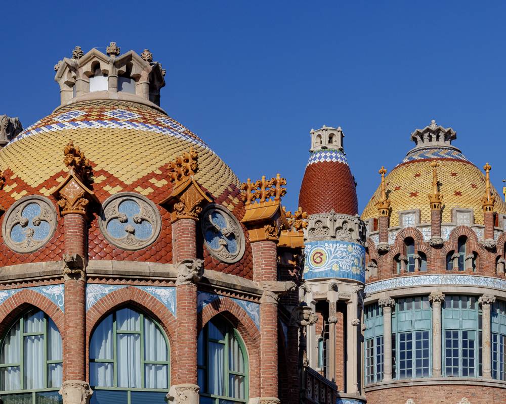 Colourful tiled domes and brick pavilions at Sant Pau Recinte Modernista under a clear blue sky
