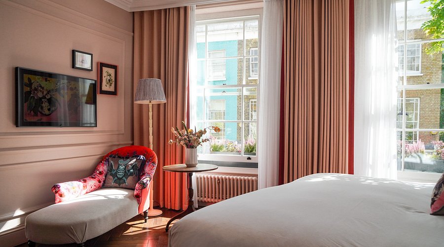 A pink bedroom with a floral chaise and tall sash windows at The Lost Poet