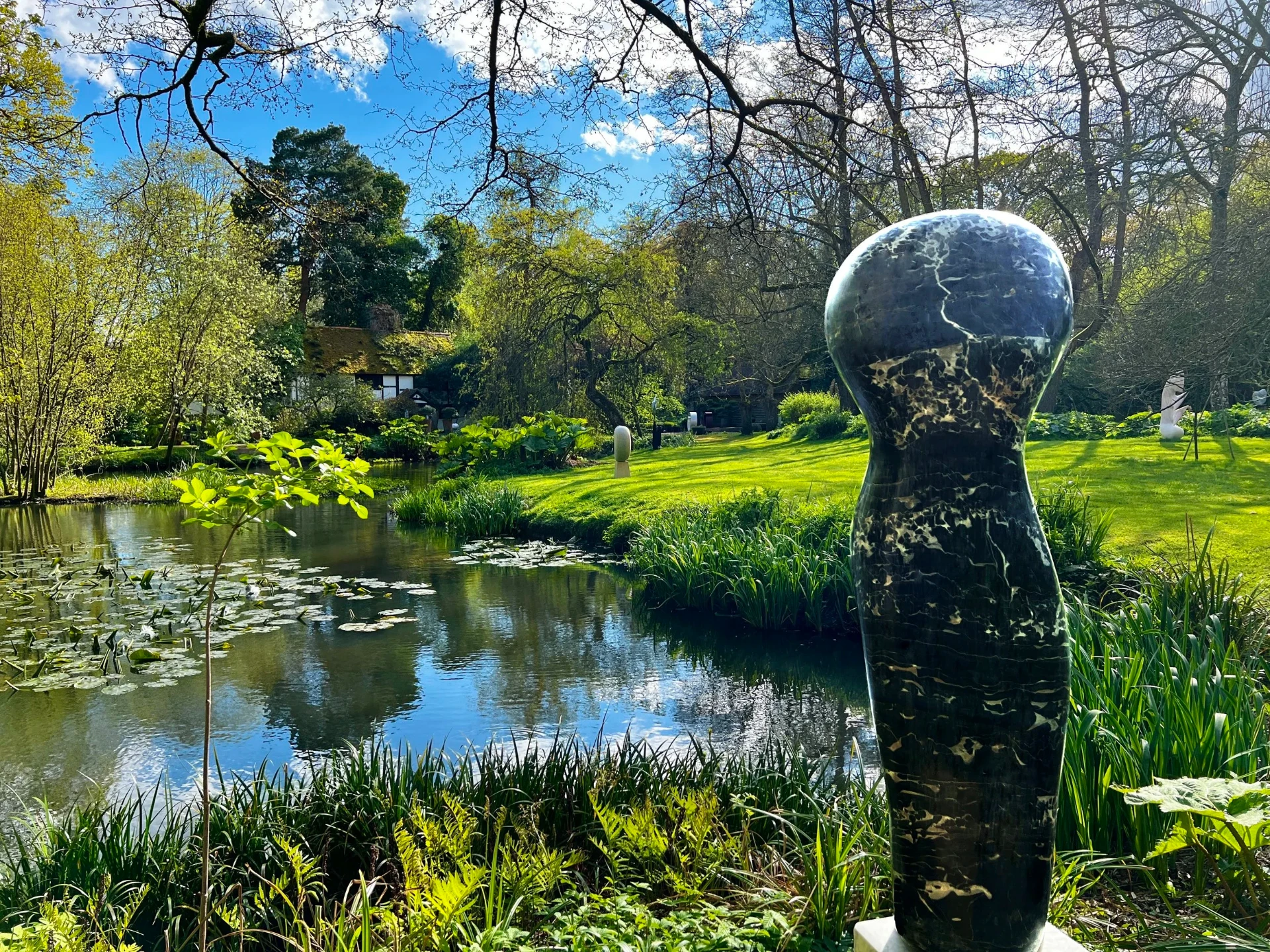 Paul Vanstone's Portorro Torso in polished marble beside the pond at the Hannah Peschar Sculpture Garden in early spring