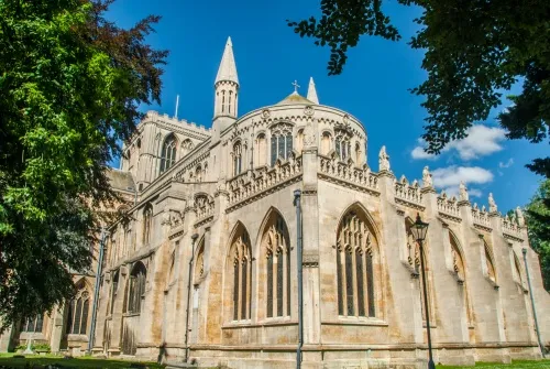 The late medieval east end of Peterborough Cathedral seen through leafy trees under a blue sky