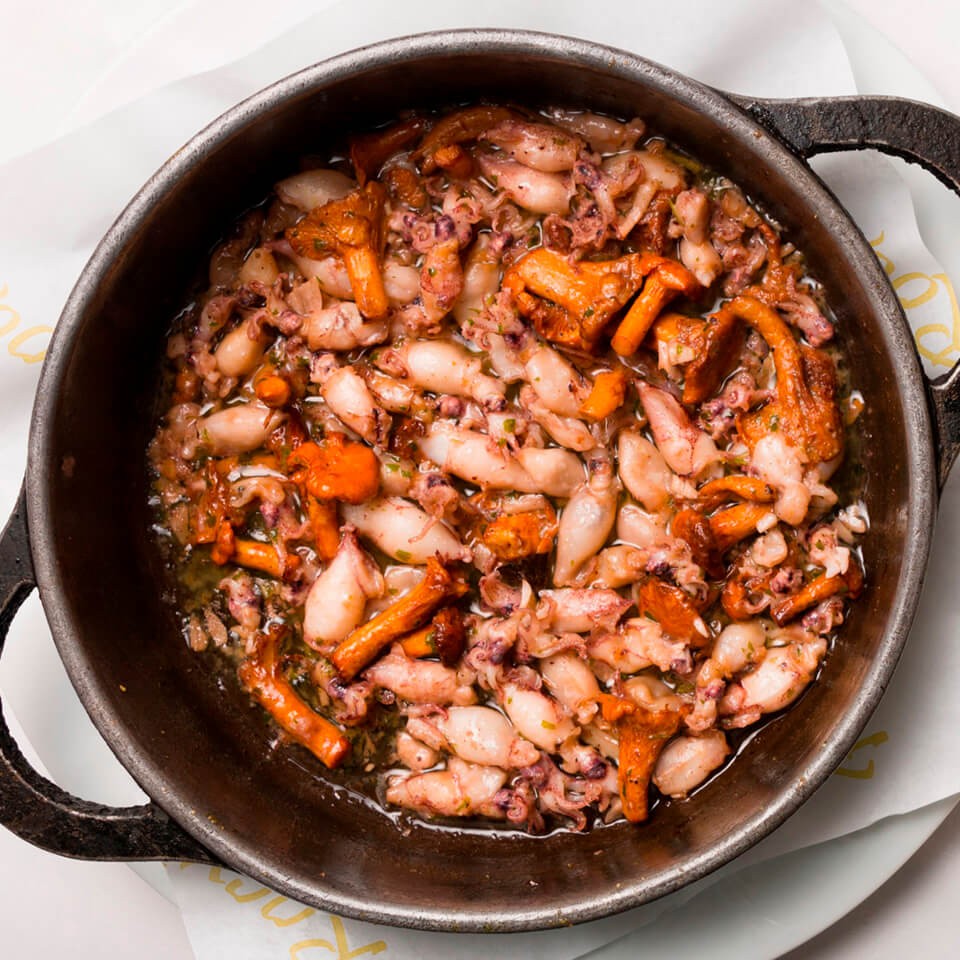 Small squid cooked in a metal pan with sauce and orange garnish at El Racó del Cargol