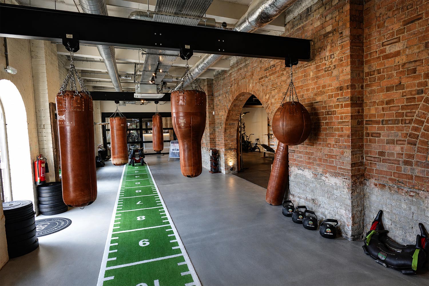 Leather punch bags hanging along the exposed brick wall of the gym at Old Station Quarter in Peterborough