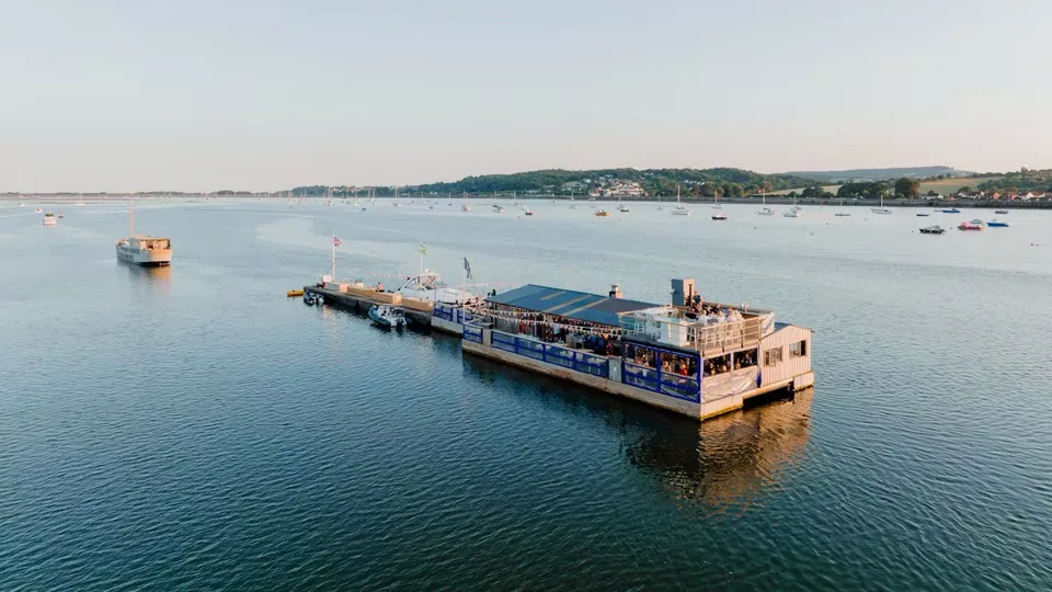 River Exe Café floating on the Exe Estuary at dusk, seen from the air with moored boats beyond