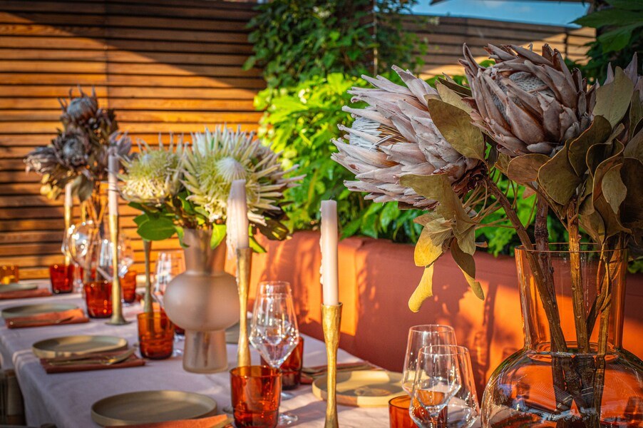 A long table laid with protea flowers, candles and amber glasses in the garden room at Gold