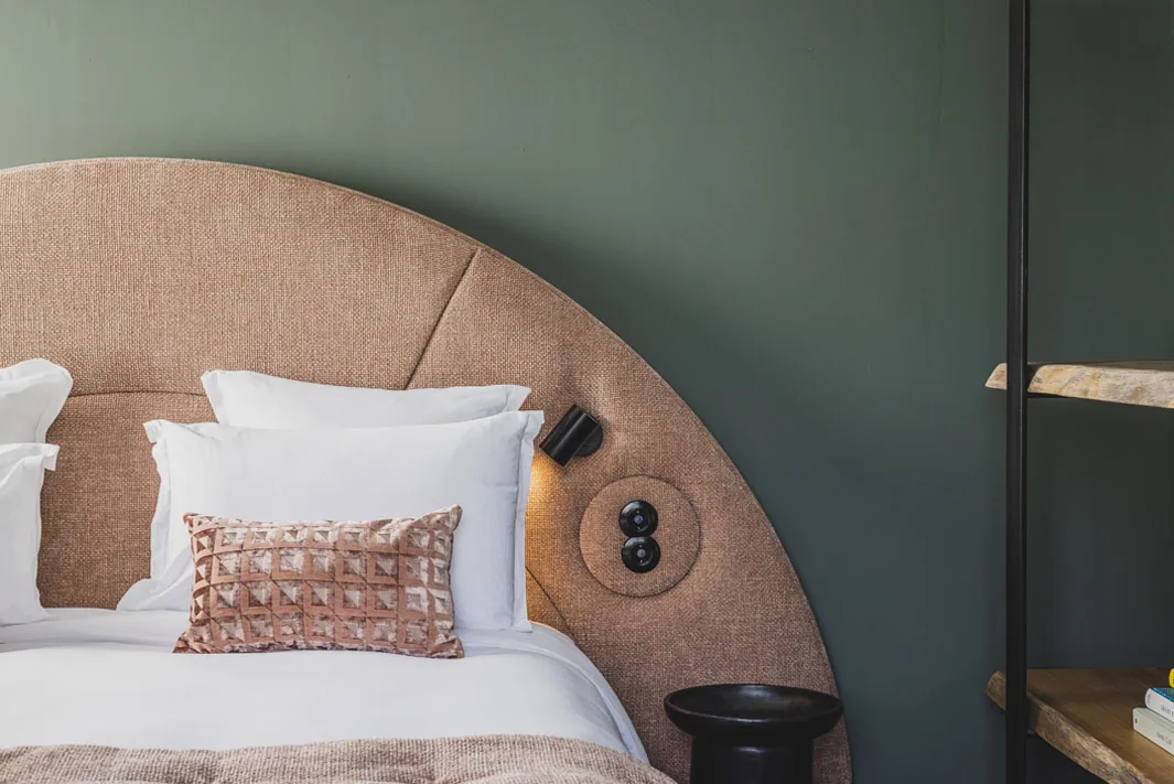 A guest room at Hôtel Le Garage — arched linen headboard against a deep green wall