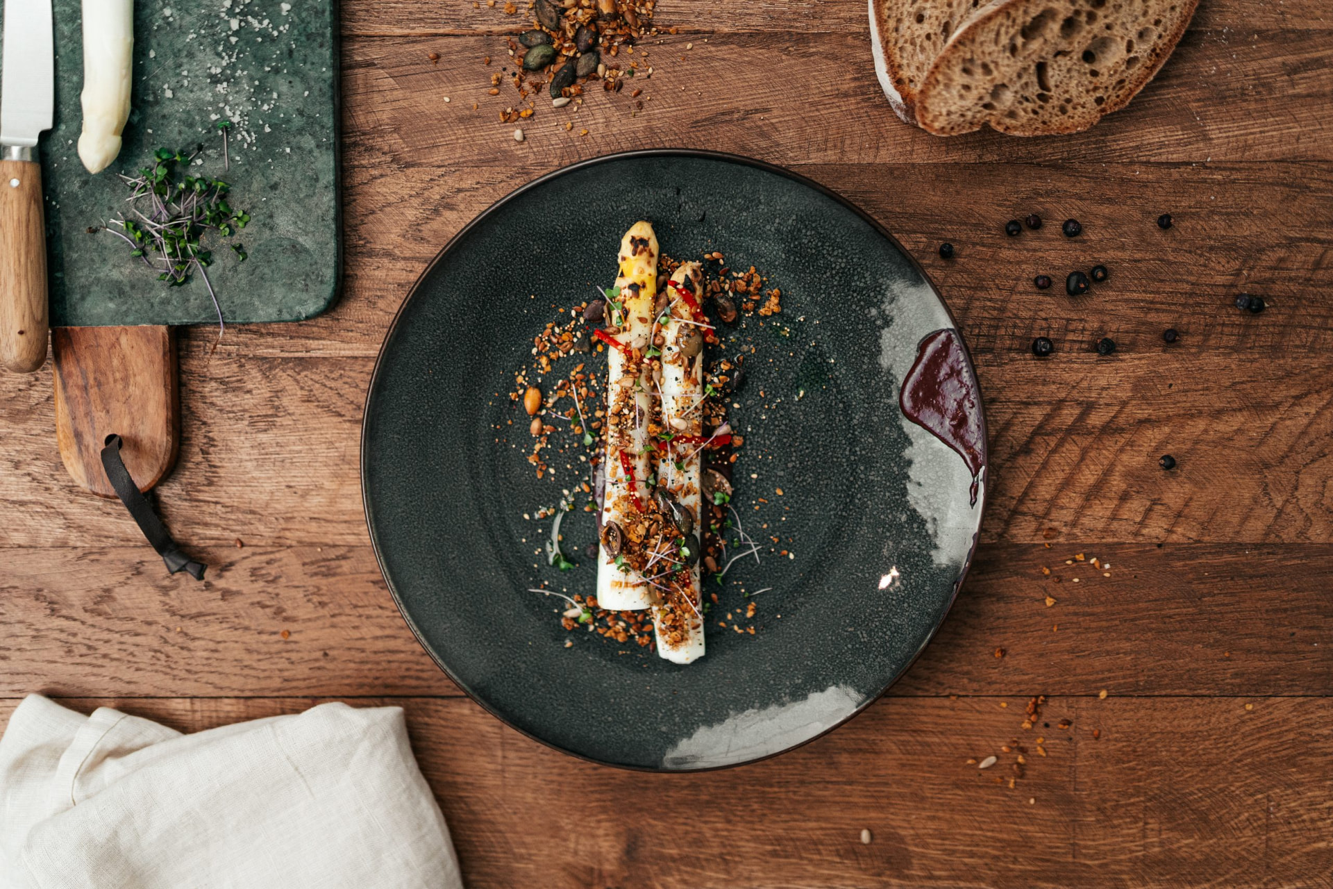 A plate of white asparagus with seeds and a dark sauce at L'Aillet, photographed from above on a wooden table